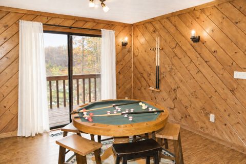 Bumper pool table by the balcony doors, with cues and stools